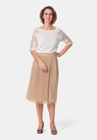 Crème blouse met kantennaden, gecombineerd met een geplisseerde beige rok. De outfit heeft een soepele textuur en een subtiele glans.