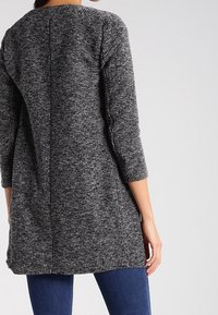 Szary i czarny sweter o teksturowanej strukturze z rękawami do trzech czwartej oraz okrągłym dekoltem, charakteryzujący się prostym krojem i detalem szwu na plecach.