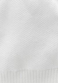 Tissu tricoté blanc avec un motif texturé, présentant une finition côtelée en bas. L'apparence générale est propre et uniforme.