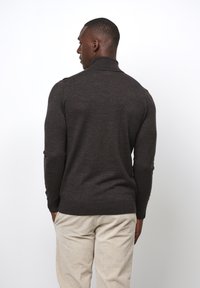 Dunkelbrauner Strickpullover mit hohem Kragen und langen Ärmeln, mit tailliertem Design. Kombinieren Sie ihn mit hellen Cordhosen.
