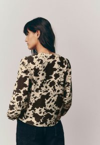 Brown and cream cow print top with long sleeves and a rounded neckline, featuring gathered shoulders and a textured fabric.