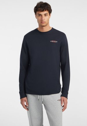 Navy long-sleeve t-shirt made of soft cotton, featuring a small red logo on the chest and fitted cuffs. Minimalist design with relaxed fit.