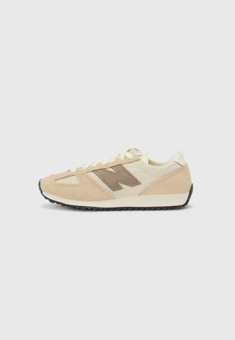 Beige og creme lavtop-sneaker med brun "N"-logo på siden, hvide snørebånd og sort mønstret sål på en lys grå baggrund.