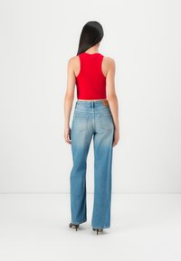 Rotes, kurzes Tanktop kombiniert mit hellblauen, weiten Jeans. Die Jeans haben einen ausgewaschenen Look, hinten Taschen und ein Lederpatch an der Taille.