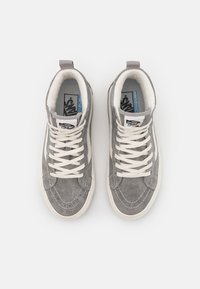 Šedé semišové vysoké tenisky s bílými tkaničkami, polstrovaným límcem a kontrastním modrým logo štítkem na jazyku. Bílá gumová podrážka.