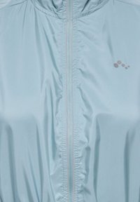 Veste légère bleu clair avec une fermeture éclair frontale ornée d'un accent rose, tissu froncé au niveau du col et petit logo sur la poitrine.