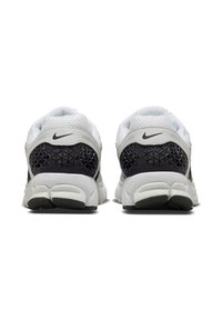 Bele in sivi Nike športni čevlji z teksturiranim črnim petnim delom, mrežastim zgornjim delom in značilnim črnim logotipom swoosh.