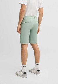 Light green shorts with a smooth texture, featuring two back pockets and a tailored fit. Worn with white socks and gray sneakers.