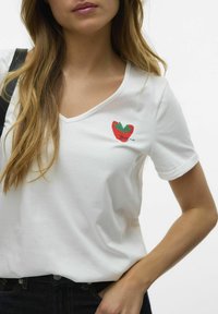 T-shirt en coton blanc avec un col en V, affichant un motif de fraise rouge et verte avec le texte "Berry nice" brodé sur la poitrine.