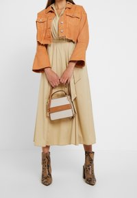 Chaqueta de mezclilla naranja recortada, vestido beige, botas de tobillo con estampado de serpiente y un pequeño bolso blanco con una correa marrón y detalles de cadena.
