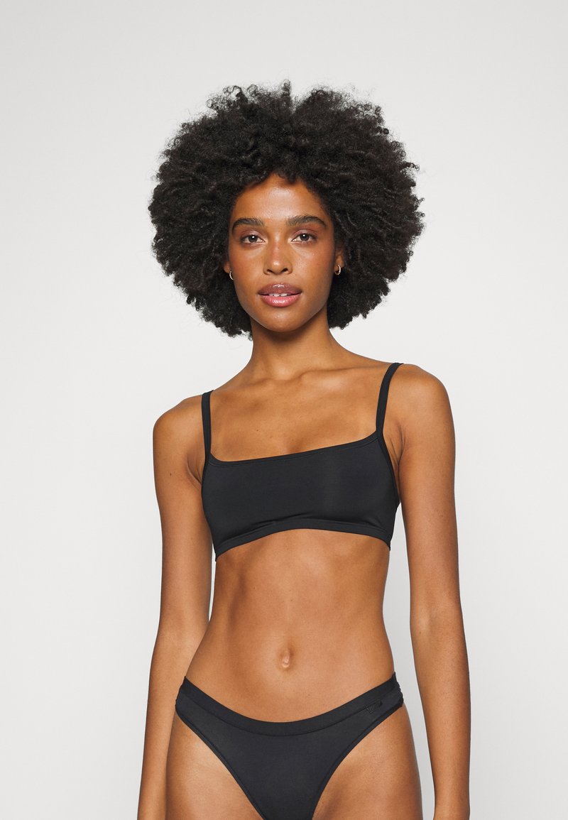 Svart bikiniset med to deler som inkluderer en rettskåret bralette med tynne stropper og matchende lavt skårne bikiniunderdeler, med glatt tekstur.