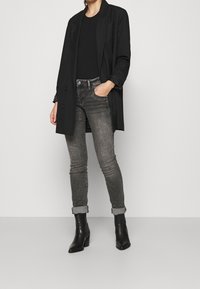 Musta bleiseri yhdistettynä tiukkaan mustaan puseroon, harmaisiin farkkuihin ja mustiin nilkkasaappaisiin. Bleiserissä on rento leikkaus ja kaksi nappia, farkut ovat hieman kuluneet.