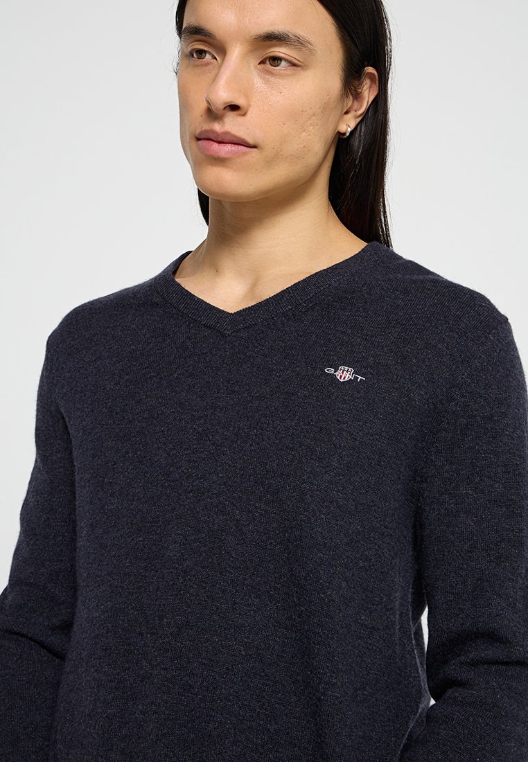 Navy V-Ausschnitt-Pullover aus weichem Strickstoff mit langen Ärmeln. Verfügt über ein kleines gesticktes Logo auf der Brust und bietet ein klassisches Design.