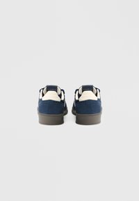 Granatowe trampki z cholewką z zamszu, kontrastowymi kremowymi akcentami i teksturowaną gumową podeszwą. Wyposażone w wyściełany kołnierz i detal z logo z tyłu.