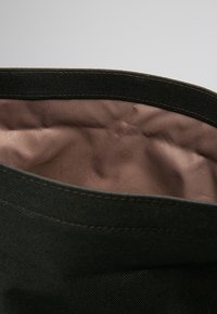 Torba na płótnie o ciemnym zewnętrzu i gładkiej, jasnobrązowej podszewce. Górna krawędź ma wzmocnione szwy.