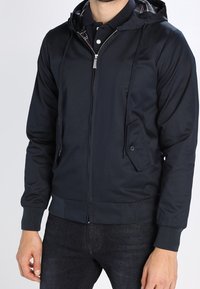 Navy zip-up jacket with a hood, featuring a textured fabric, side pockets, and a plaid interior lining. Ribbed cuffs and waistband.