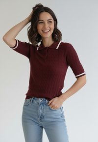 Bordowa dzianinowa koszulka polo z białym paskowanym kołnierzykiem i krótkimi rękawami, zestawiona z jasnoniebieskimi dżinsami z wysokim stanem.