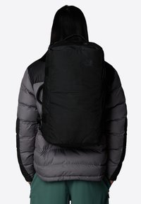 Svart ryggsäck tillverkad av hållbart tyg, med en rektangulär design, justerbara remmar och en logotypdetalj på framsidan.