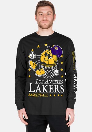Mann trägt ein schwarzes langärmeliges Los Angeles Lakers Shirt mit einer Cartoon-Basketballfigur mit Cap, die auf einem Basketballkorb sitzt.