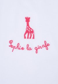Un tessuto bianco presenta una silhouette di giraffa ricamata in rosa sopra il testo "Sophie la girafe" in un font corsivo rosa coordinato.