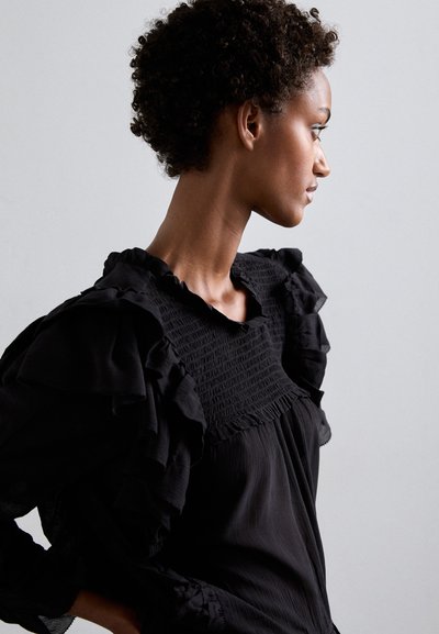 Black blouse featuring a smocked bodice, ruffled sleeves, and a round neckline. The fabric appears lightweight with a slightly textured finish.