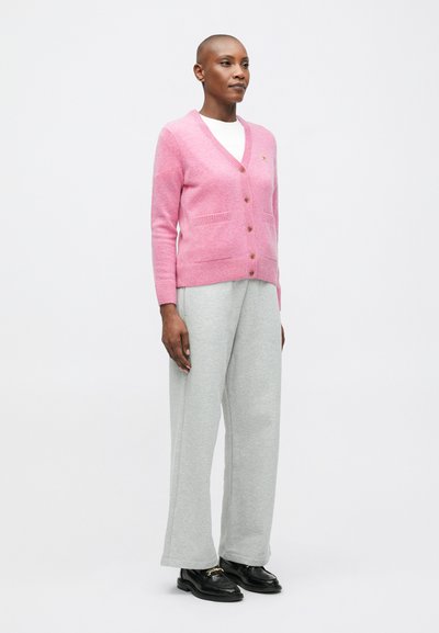 Cardigan roz cu decolteu în V, nasturi din lemn și buzunare frontale, purtat cu pantaloni largi gri și pantofi negri. Textură netedă.