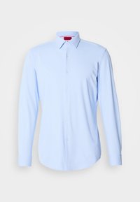Chemise bleu clair à manches longues boutonnée avec un col pointu et des boutons blancs sur fond blanc.