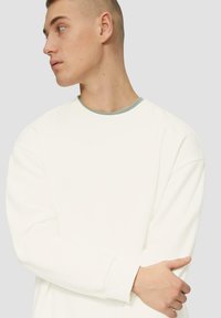 Biała bluza z okrągłym dekoltem i długimi rękawami. Posiada jasny wykończenie przy dekolcie. Miękka tekstura, luźny krój.