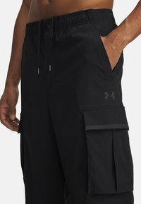 Black cargo shorts with a textured fabric, elastic waistband, and side pockets. Features a contrasting logo on the front pocket.