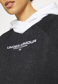 Sudadera negra con capucha blanca, que presenta una textura jaspeada. Logo bordado de "UNDER ARMOUR" en blanco en la parte frontal.