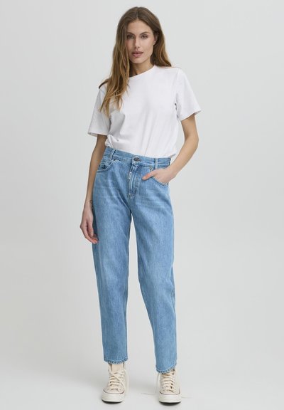 Vaqueros de tiro alto azul claro con un ajuste relajado, dos bolsillos frontales y cierre de botón. Combinados con una camiseta básica blanca de cuello redondo.