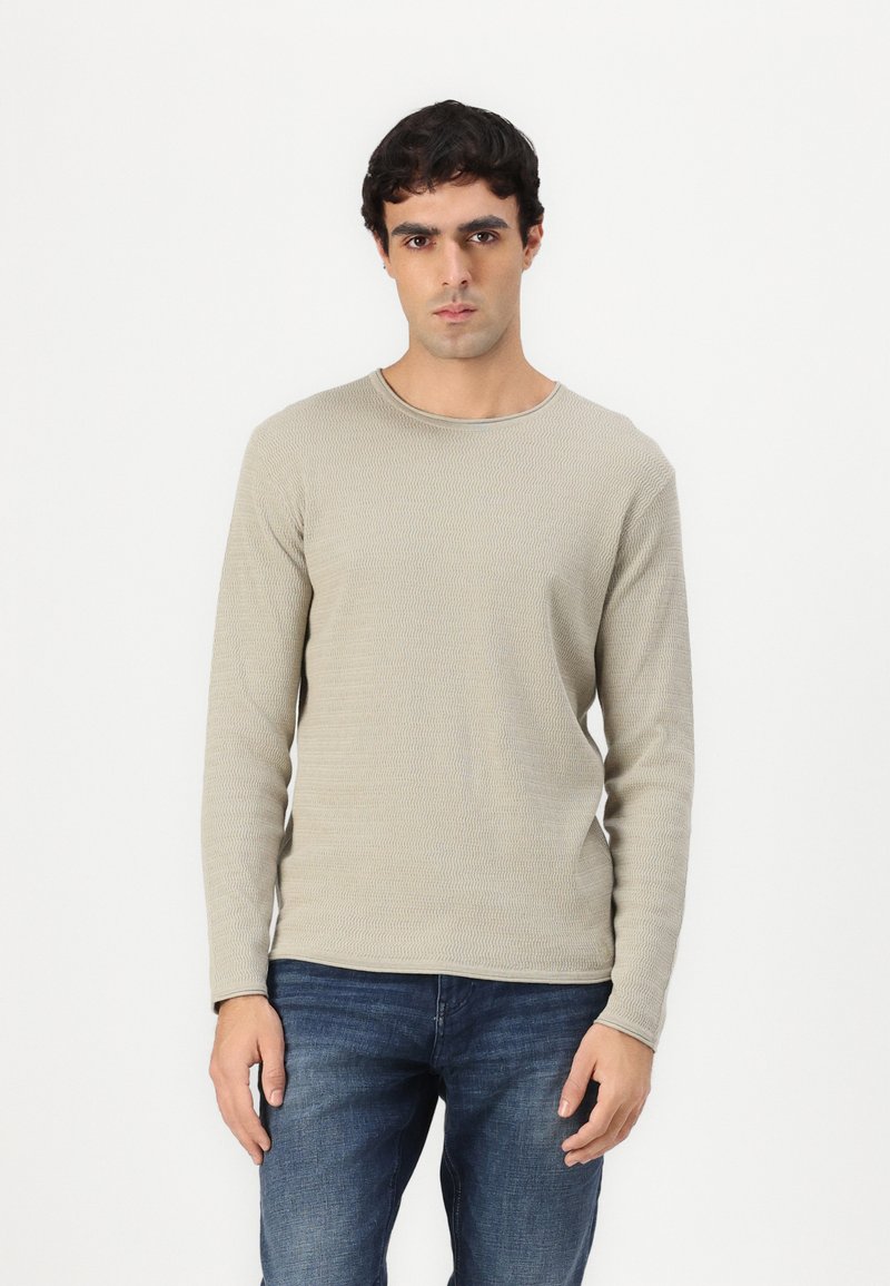Camisa de manga larga en color beige claro con un cuello redondo, combinada con jeans oscuros de diseño texturizado.