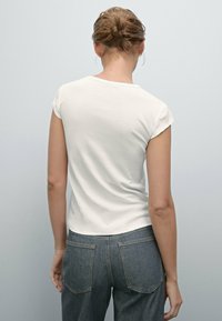 Witte katoenen t-shirt met korte mouwen, getailleerde snit, golvende halslijn, gedragen met donkerblauwe denim jeans met achterzakken en contrasterende stiksels.