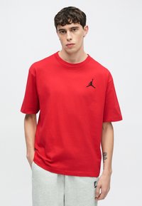 Punainen puuvillainen t-paita, jossa on lyhyet hihat ja pyöreä kaula-aukko. Vasemmassa rinnassa musta Jumpman-logo. Yhdistetty harmaisiin verkkarihousuihin.