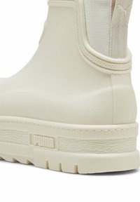 Botte de cheville Puma de couleur crème avec semelle texturée, panneau latéral élastique et languette à l'arrière pour un enfilage facile.