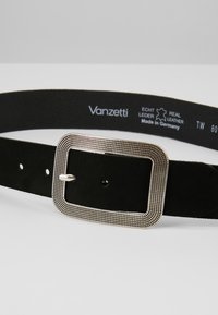 Cinturón de cuero negro con una hebilla rectangular plateada texturizada. Presenta múltiples agujeros de ajuste y un lado inferior suave con marca.