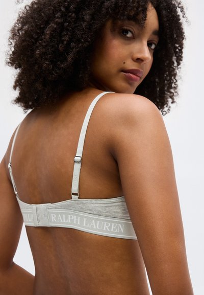 Γυναίκα με σγουρά μαλλιά που φοράει ένα ανοιχτό γκρι σουτιέν με ρυθμιζόμενες τιράντες και το λογότυπο "RALPH LAUREN" στην πίσω ζώνη.