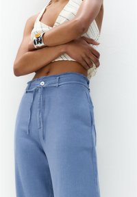 Jasnoniebieskie lniane spodnie z postrzępionym pasem, regulowanym sznurkiem, kieszeniami z przodu i pojedynczym zapięciem na guzik. Teksturowana tkanina.