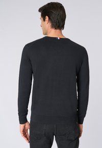 Maglione lavorato a maglia di un blu scuro con maniche lunghe e orlo a coste. Presenta un piccolo tag tri-colore sul retro del collo. Texture morbida e forma aderente.