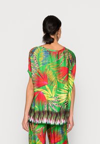 Top multicolore con base verde e vivaci motivi tropicali rossi e gialli. Vestibilità ampia con maniche corte e orlo a gradiente sottile.