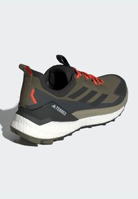 Dark green running shoe with black and gray accents. Features textured upper, bright orange laces, thick white sole, and heel tab.