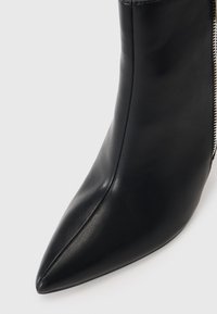Svarte lær ankelstøvler med spiss tå, glatt tekstur og glidelås på siden for lukking. Minimalistisk design, ingen synlige dekorasjoner.