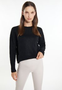 Pulover negru din tricot cu mâneci lungi, decolteu rotund și tiv cu dungi. Textură netedă, croi lejer. Asortat cu pantaloni de culoare deschisă.