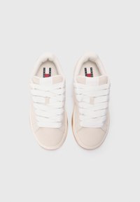 Beige sneakers with a smooth fabric upper and rubber outsole. Features white textured laces and logo on the tongue in dark blue and red.