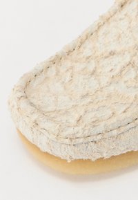 Beige textilcipő, textúrált felülettel és kerek orral, látható varrással és világos színű, sima talppal.