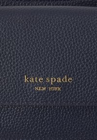 Portefeuille en cuir bleu marine avec une finition texturée, arborant un logo doré en relief portant la mention "kate spade NEW YORK" et des lignes épurées.