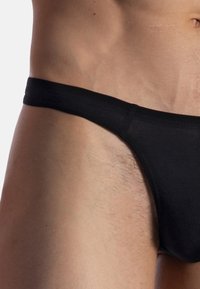 Schwarzer Tanga aus weichem Stoff, mit schmalem Bund und minimaler Bedeckung, entworfen für einen engen Sitz. Die Textur wirkt glatt.