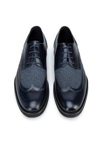 Scarpe in pelle blu scuro con un motivo a chevron sulla parte superiore. Presentano una punta liscia con bordi ondulati e lacci. Suole nere.