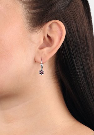 Pendiente de aro de plata con un diseño trenzado y una pequeña cuenta multicolor. El pendiente cuelga de un gancho delgado.