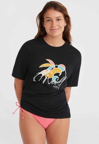 Sort t-shirt med et farverigt grafisk design med tropiske blade. Båret med pink bikiniunderdel, der viser en afslappet pasform og rund hals.